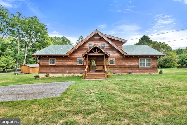 cabin with log siding, a shingled roof, and a front lawn
