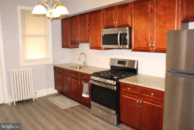 kitchen featuring dark brown cabinets, radiator heating unit, a sink, backsplash, and stainless steel appliances