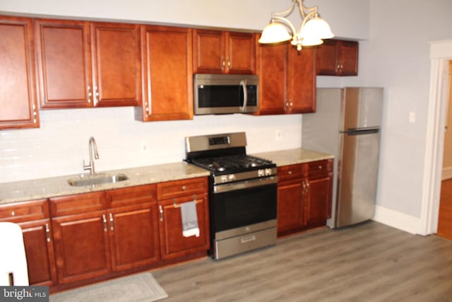 kitchen featuring light stone countertops, a sink, light wood-style flooring, stainless steel appliances, and backsplash