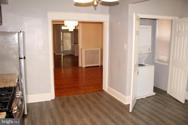 kitchen with baseboards, stainless steel gas range oven, stacked washer / drying machine, and dark wood-type flooring