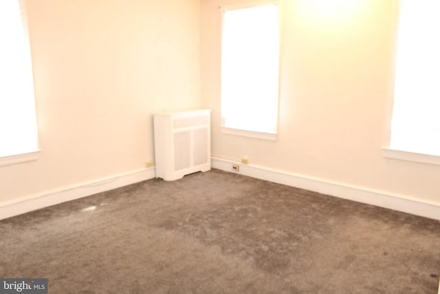 carpeted empty room with plenty of natural light, radiator, and baseboards