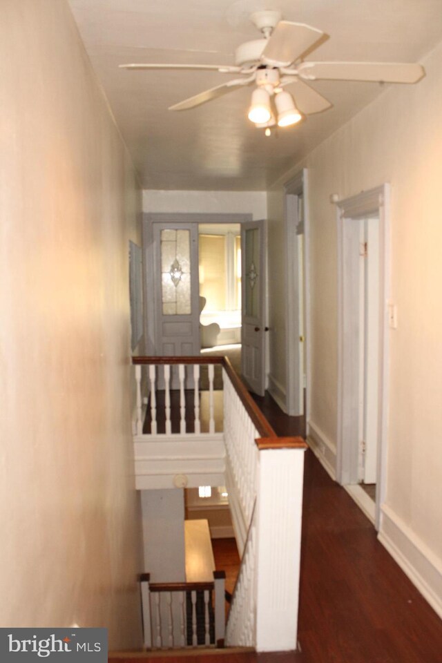 hallway with baseboards, wood finished floors, and an upstairs landing