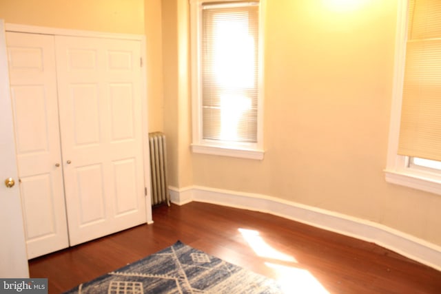 unfurnished bedroom with baseboards, dark wood-style floors, radiator heating unit, and multiple windows