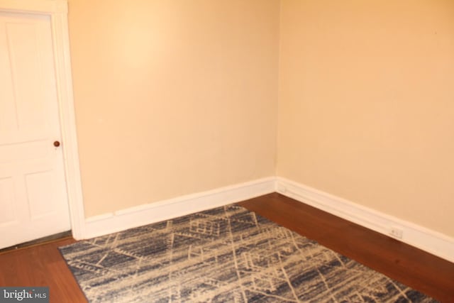 empty room with baseboards and dark wood-type flooring