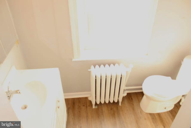 bathroom featuring wood finished floors, baseboards, radiator heating unit, and toilet