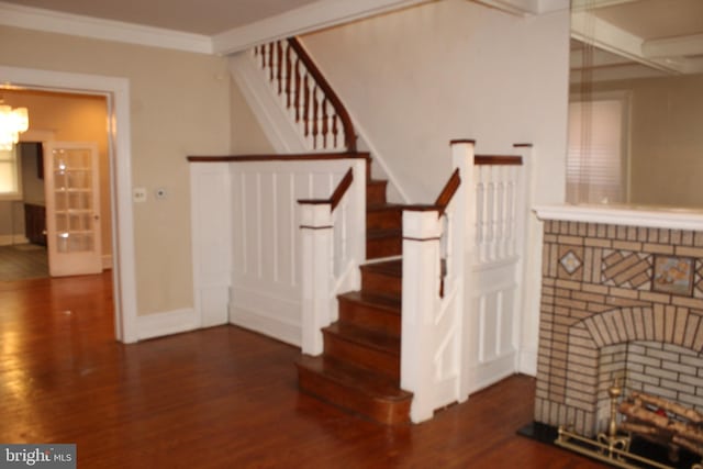 staircase with crown molding, a brick fireplace, wood finished floors, baseboards, and a chandelier
