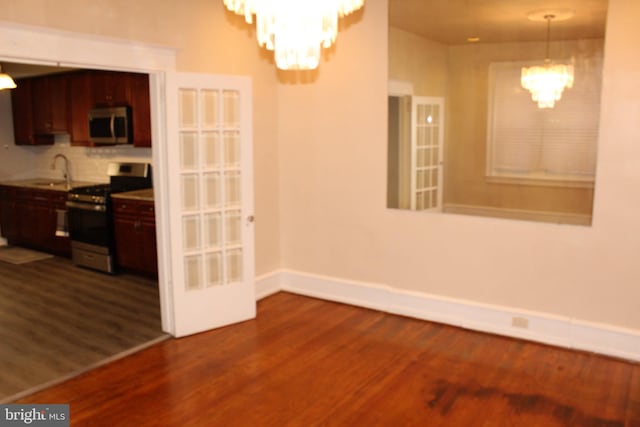 unfurnished dining area with baseboards, a notable chandelier, dark wood-style floors, and a sink