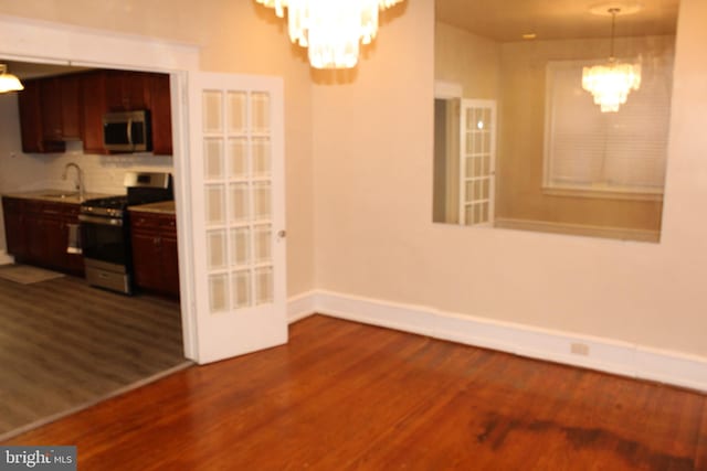 unfurnished dining area featuring baseboards, a sink, dark wood-style flooring, and a notable chandelier