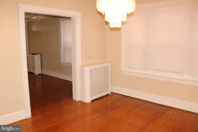 unfurnished dining area with baseboards, a notable chandelier, radiator heating unit, and wood finished floors
