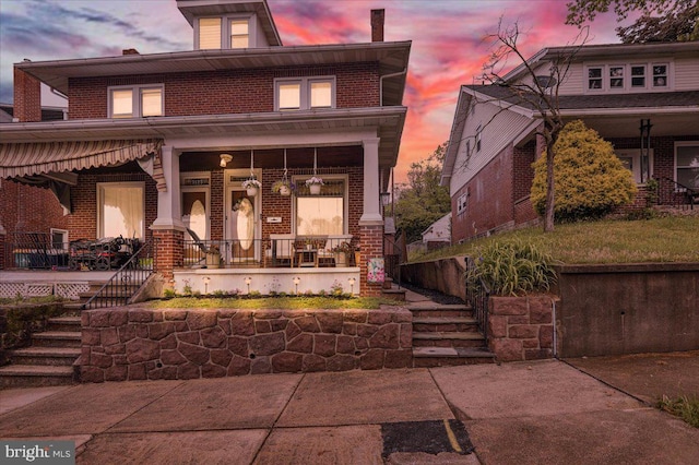 back of property at dusk with covered porch, brick siding, and stairway
