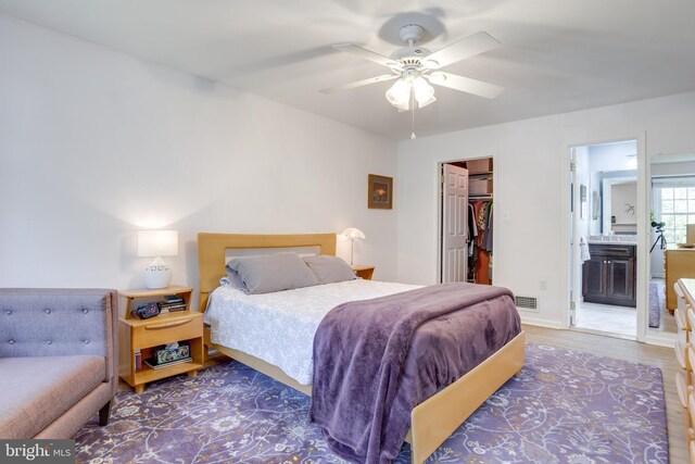 bedroom featuring ceiling fan, visible vents, wood finished floors, a spacious closet, and ensuite bathroom