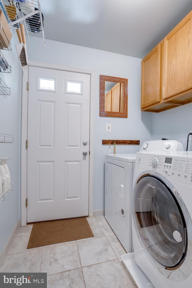 clothes washing area featuring light tile patterned floors, baseboards, washing machine and dryer, and cabinet space