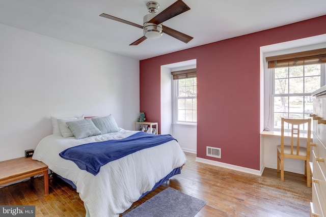bedroom with baseboards, ceiling fan, wood finished floors, and visible vents