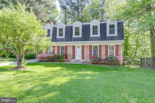 view of front facade with fence, a shingled roof, a front lawn, brick siding, and a chimney
