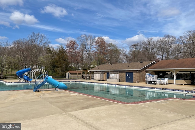 community pool with fence, a water slide, and a patio area