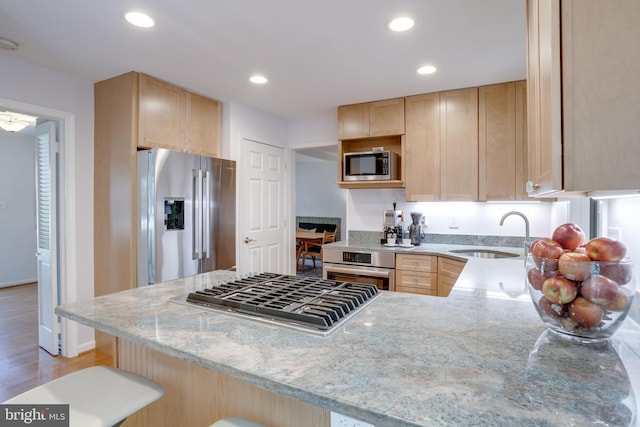 kitchen featuring light brown cabinetry, light stone countertops, a sink, a peninsula, and stainless steel appliances