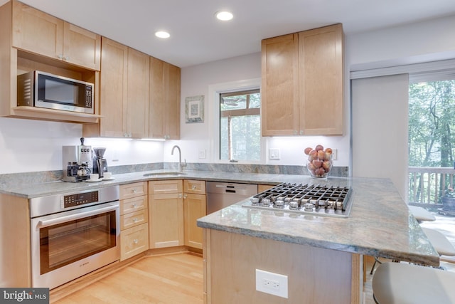 kitchen featuring a sink, light brown cabinets, stainless steel appliances, a peninsula, and light wood-type flooring