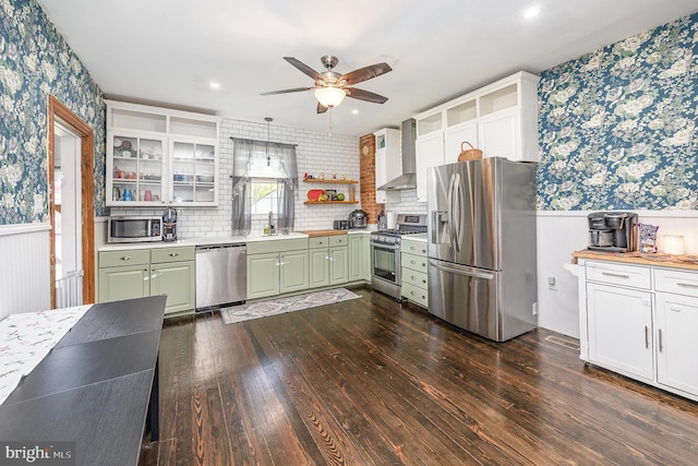 kitchen featuring wainscoting, green cabinetry, stainless steel appliances, wallpapered walls, and wall chimney exhaust hood