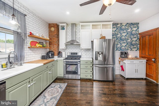 kitchen with wall chimney range hood, light countertops, green cabinetry, a sink, and appliances with stainless steel finishes