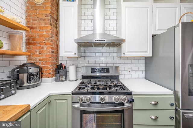 kitchen featuring wall chimney range hood, green cabinetry, appliances with stainless steel finishes, open shelves, and backsplash