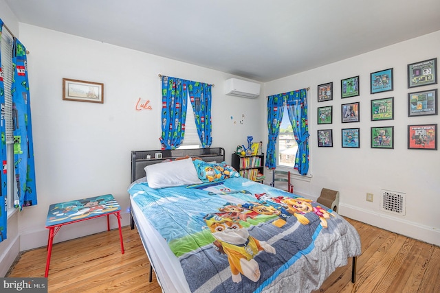 bedroom featuring baseboards, a wall unit AC, wood finished floors, and visible vents