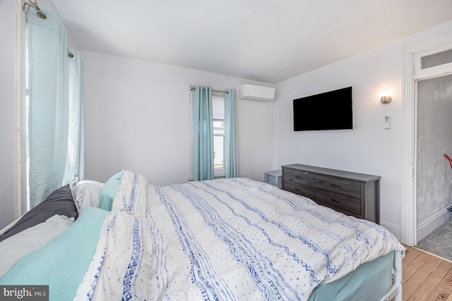 bedroom featuring baseboards, a wall mounted air conditioner, and wood finished floors