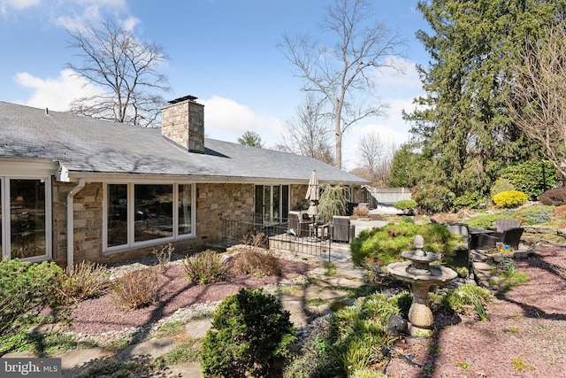 back of house featuring a chimney, stone siding, and a patio