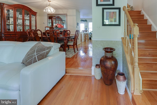 living room featuring stairs, baseboards, a chandelier, and light wood-type flooring