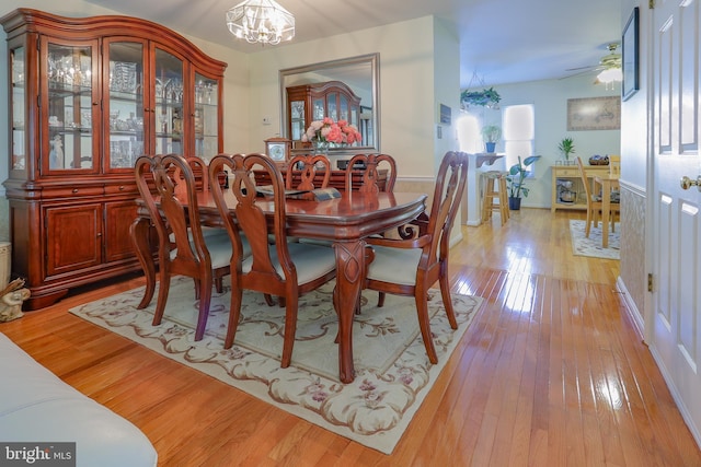 dining area featuring baseboards, light wood-style flooring, and ceiling fan with notable chandelier