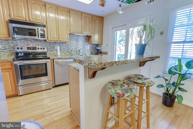 kitchen with backsplash, stainless steel appliances, a breakfast bar, and light wood finished floors