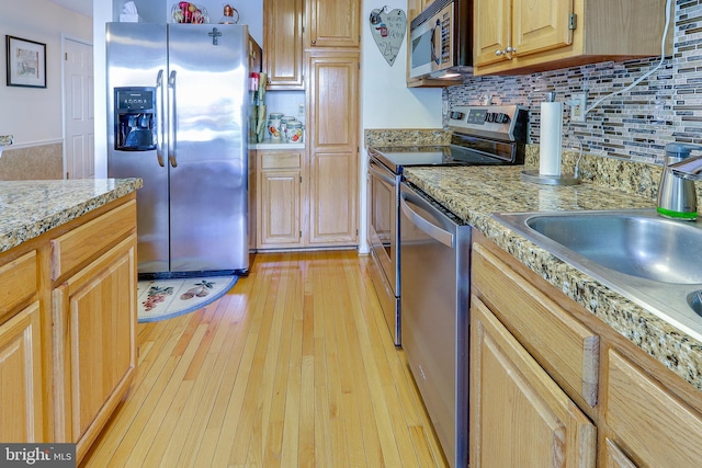 kitchen with stainless steel appliances, a sink, light wood-style flooring, and tasteful backsplash