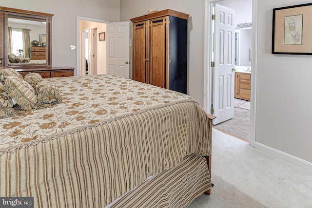 bedroom with baseboards, light colored carpet, and ensuite bath