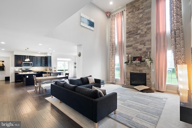living room featuring a high ceiling, a fireplace, recessed lighting, and wood finished floors