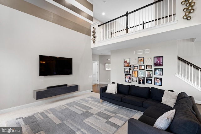 carpeted living room featuring stairs, baseboards, visible vents, and a towering ceiling