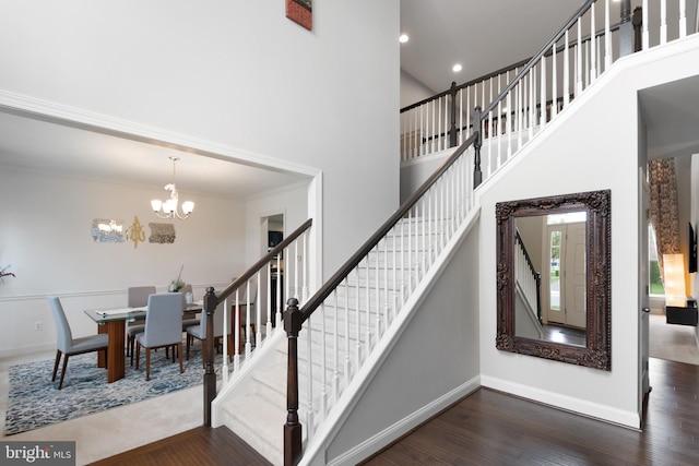 stairway with baseboards, a notable chandelier, wood finished floors, and a towering ceiling