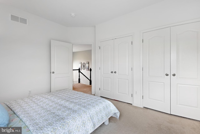 bedroom featuring multiple closets, light carpet, and visible vents