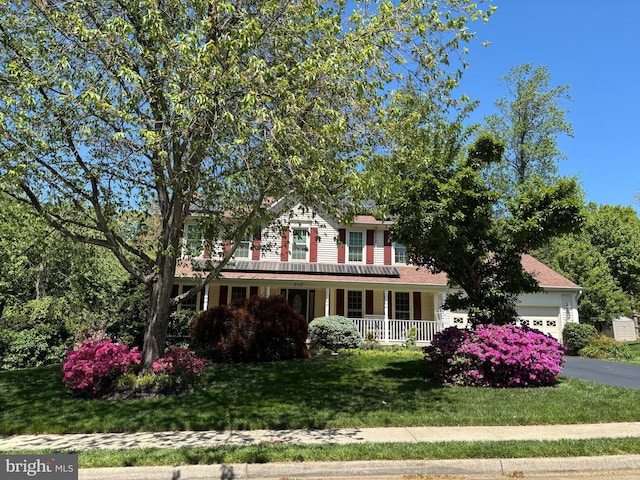 colonial home featuring covered porch, a front yard, and a garage