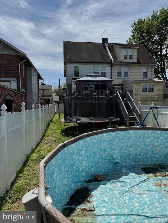 view of swimming pool with a gazebo, a fenced backyard, a trampoline, and a lawn