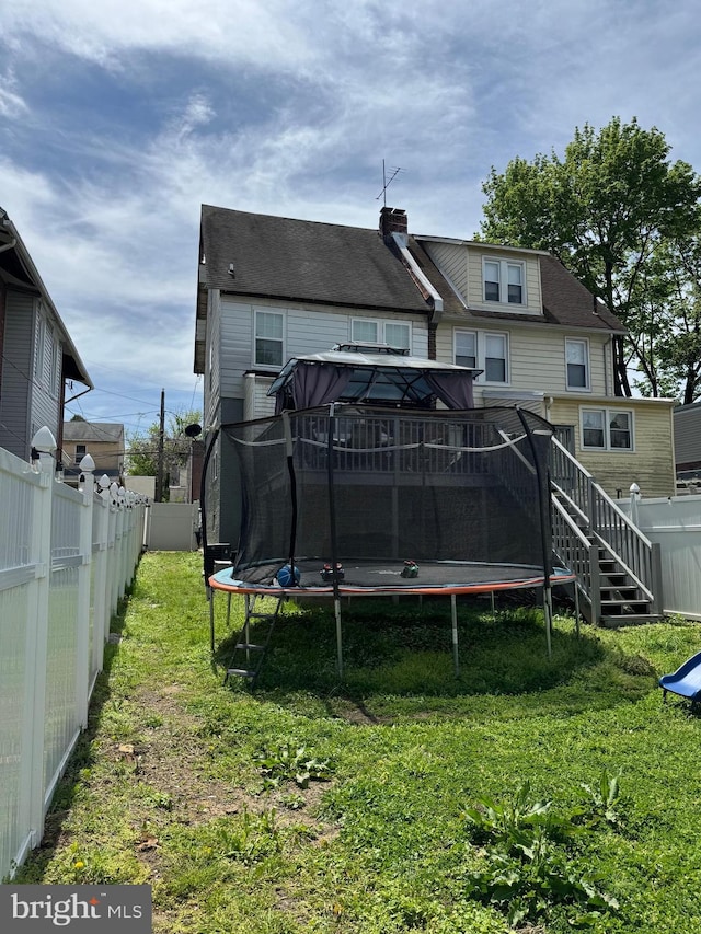 back of property with a lawn, a trampoline, and a fenced backyard