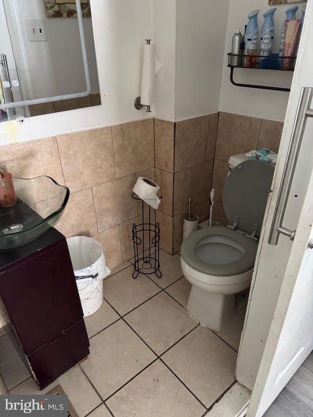 bathroom with wainscoting, tile patterned floors, toilet, and tile walls