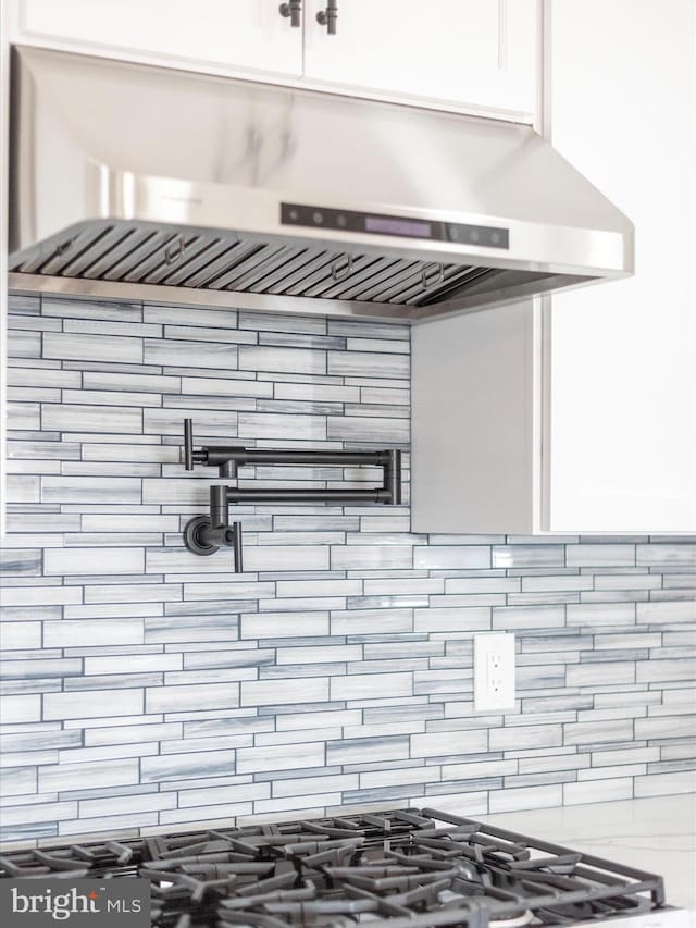 interior details with white cabinetry, under cabinet range hood, and tasteful backsplash