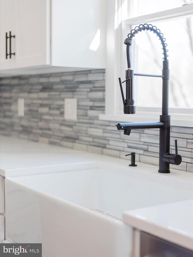 room details with backsplash, white cabinetry, a sink, and light countertops