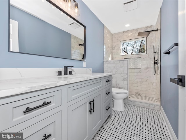bathroom featuring vanity, a tile shower, toilet, and visible vents