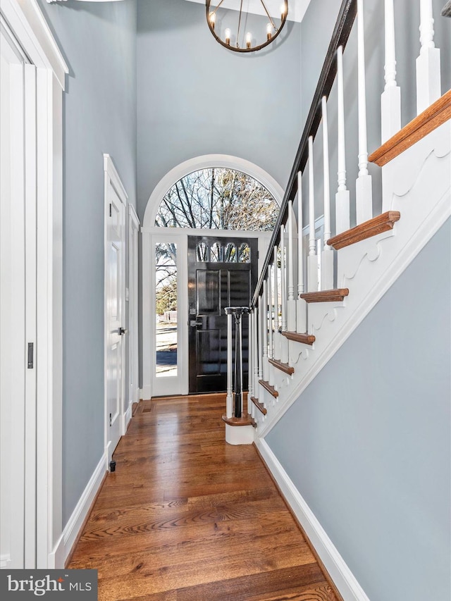 entryway featuring a high ceiling, a notable chandelier, stairs, baseboards, and wood finished floors