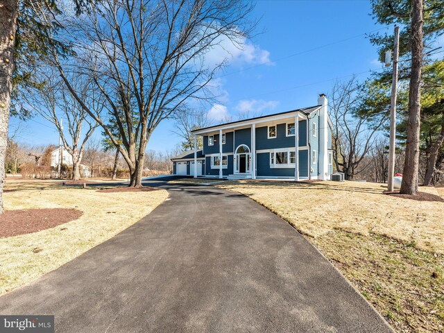 view of front of house featuring an attached garage, a chimney, a porch, central air condition unit, and driveway
