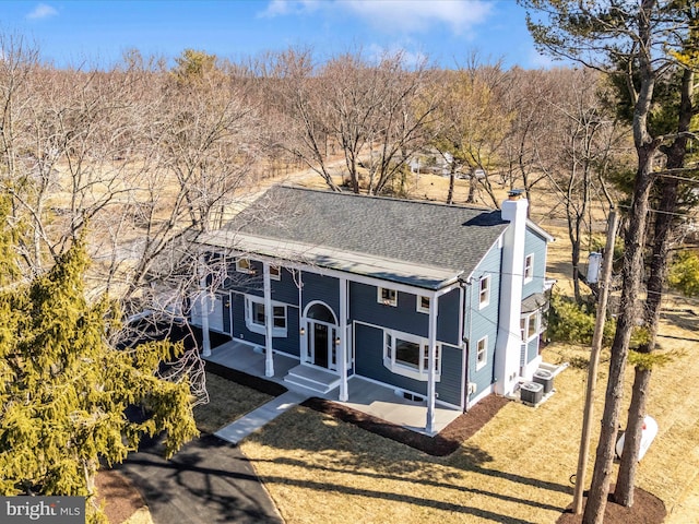 view of front of home with a shingled roof, central AC, covered porch, and a chimney