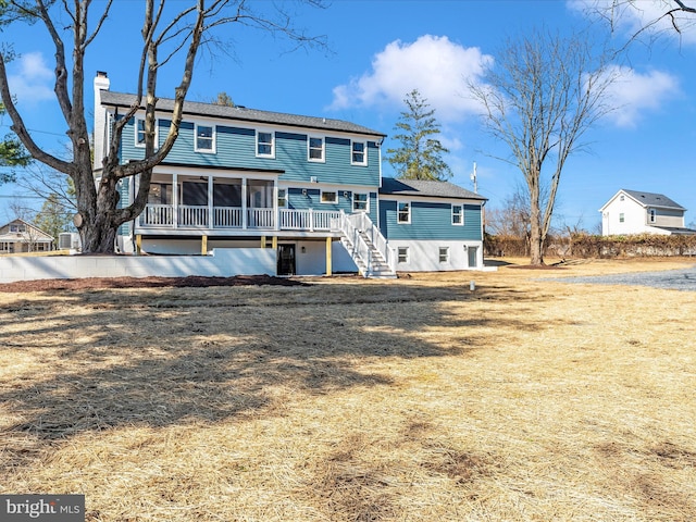 back of property with a chimney, a wooden deck, a sunroom, a shingled roof, and stairs