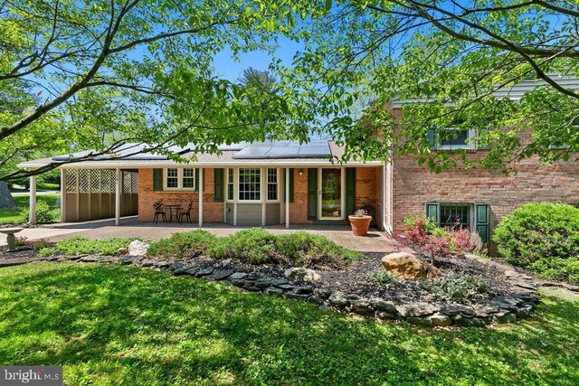 rear view of house with brick siding, an attached carport, a porch, roof mounted solar panels, and a yard