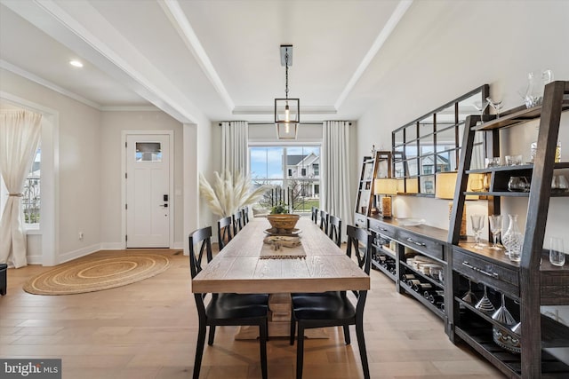 dining area featuring baseboards, crown molding, a raised ceiling, and light wood finished floors