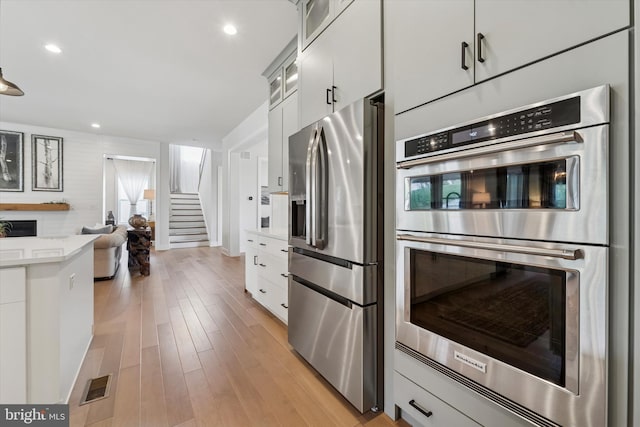 kitchen featuring visible vents, appliances with stainless steel finishes, light countertops, open floor plan, and glass insert cabinets